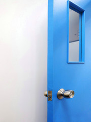 Blue door with metal knob. There is a small glass window opened in front of white concrete wall. Close up view - Copy space for add text is on the left.