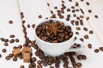 grains of coffee in a white porcelain cup and scattered on a white wooden table, brown sugar and tubby