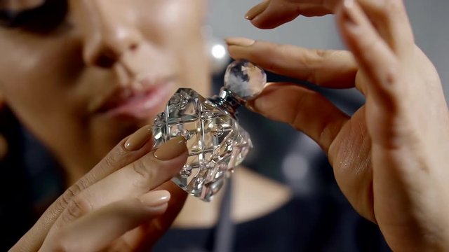 Close up shot of charming woman holding small glass bottle of perfume.