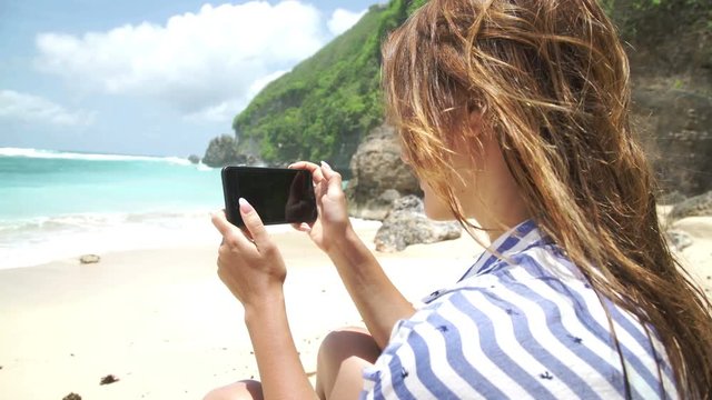 Beautiful woman taking photo using phone on beach Bali Indonesia