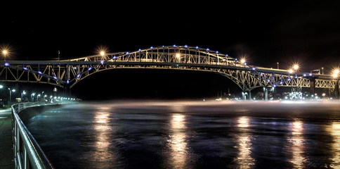 International Border Crossing. The International Blue Water Bridge illuminated at night. The Bridge spans the St. Clair River and connects Pt. Huron, Michigan, USA and Sarnia, Ontario, Canada.