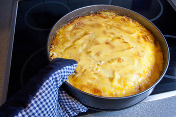 The cook takes from the oven baked fish, hake fillet cooked with carrots, onions, cheese, apple and mayonnaise.