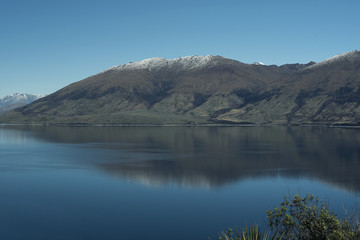 Naklejka na ściany i meble Paisaje de montañas frente a un gran lago donde se reflejan. Cielo azul despejado.