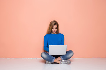Naklejka premium Serious woman working with laptop while sitting on floor isolated. Woman typing on laptop computer while sitting on the floor with legs crossed.
