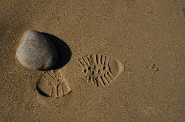 Obraz premium A shoe mark on sand near a stone on sand