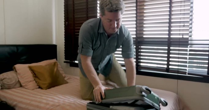 Man trying to close his travel bag drops it on the floor while packing