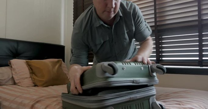 Man struggling to close his overpacked carry on luggage while traveling