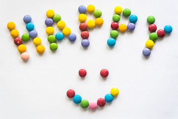 The word "happy" and smile sign is laid out on a white background from multi-colored drageess. Letters from a sweet colored dragee.
