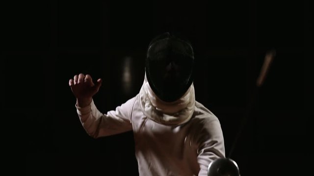 A man dressed for fencing wears a mask and is preparing a rapier. Close-up. Camera movement from the bottom up