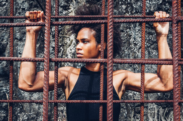 All power to the people, afro american athlete girl with strong arms after workout behind iron bars