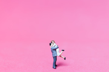 Miniature couple hugging on pink background, valentine concept