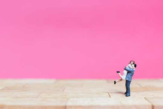 Miniature couple hugging on pink background, valentine concept