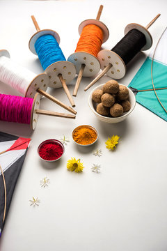 happy Makar Sankranti Festival - Tilgul or Til ladoo in a bowl or plate with haldi kumkum and flowers with Fikri /Reel/Chakri /Spool with colourful thread or manjha and kite over plain background