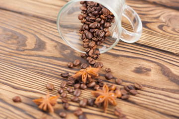 Lot of fried coffee beans and three anises poured out of transparent glass for mulled wine with handle on old wooden rustic brown planks