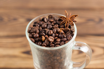 Lot of fried coffee beans and one anise in transparent glass for mulled wine with handle on old wooden rustic brown planks. Close-up
