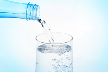 Pouring water from bottle into glass on white background.