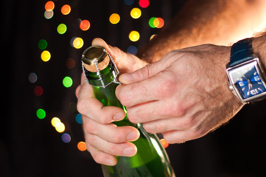 Opening a bottle of sparkling wine like champagne, a man's hand with a watch, New Year's lights, happy new year and Christmas, celebration 2018.