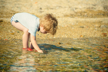 Boy looking for stones or small fishes in the sea. Summer vacation near sea. Tourism with children. Pleasure of walking on the water. Small researcher and searcher, small explorer