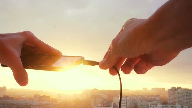 Detail of stereo jack being plugged into smartphone with sunset on background