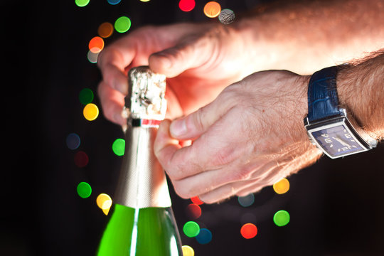 Opening a bottle of sparkling wine like champagne, a man's hand with a watch, New Year's lights, happy new year and Christmas, celebration 2018.