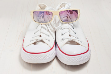 A pair of new white hipster sneakers in sunglasses on an old wooden background, casual life style, top and front view