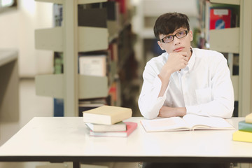 Young student study hard in library. Asian male university student doing study research in library with books and on desk and smiling. For back to school education concept.