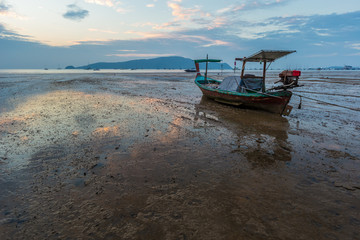 Fototapeta na wymiar Fishing boat at the beach (long-tail boats) in low water and the beautiful sunrise at Phuket Island, Thailand.
