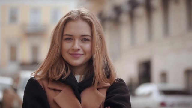 Slow motion street shot of cute caucasian woman wearing beige coat having good mood captured while spending time in city centre in autumn. Film look