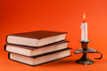 Candle burning in candlestick and three old books isolated on orange background
