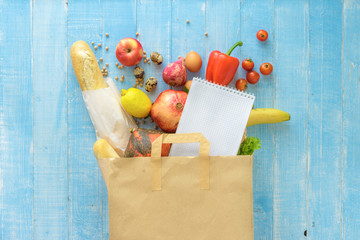 Paper bag different fresh health food notebook on wooden background