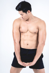 Fitness and health concept. Fit sport man flexing his body showing his six packs, isolated on white background. Half naked Asian chinese lean muscular male wearing a black shorts.