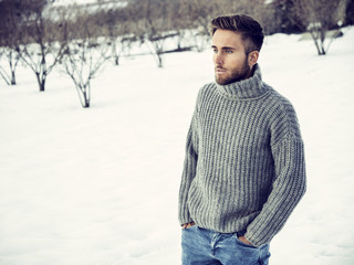 Handsome young man outdoor in winter fashion, wearing black coat and woolen scarf in snow environment