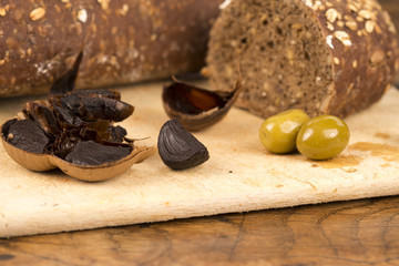 Black garlic and olives with bread on a chopping board