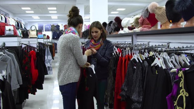 Two young beautiful girls choose clothes in a fashionable boutique. Girls carefully look at the clothes and examine it.