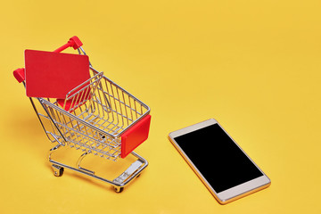 shopping trolley cart with credit card and phone on yellow backgroud