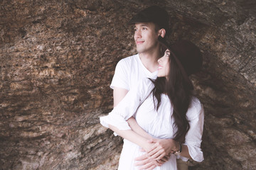 Couple holding each other with rocky beach background. Young happy interracial couple on beach holding each other. Asian woman, Caucasian man. Young mixed race romance concept.