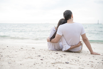 Fototapeta na wymiar Couple holding each other on beach. Young happy interracial couple on beach holding each other sitting down. Asian woman, Caucasian man. Young mixed race romance concept.