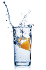 Slice orange dropping into water glass on white background