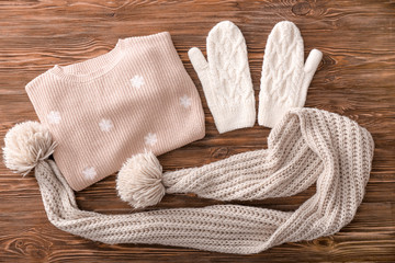 Warm knitted clothes on wooden background. Seasonal female wardrobe