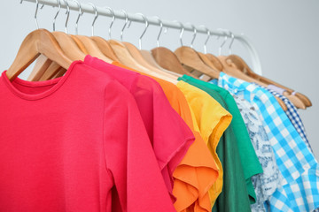 Stylish clothes hanging on wardrobe stand against light background