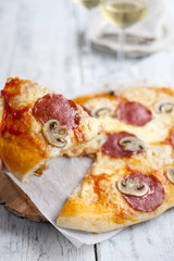pizza with salami and mushrooms on a white wooden background and two glasses of white wine