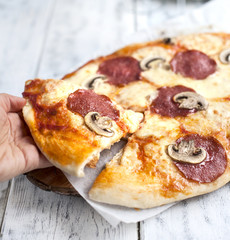 Pizza with salami and mushrooms on a white wooden background