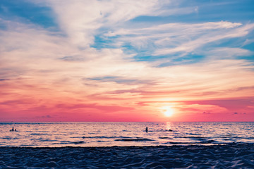 Fototapeta premium Coast of the sea at colorful sunset, Koh Chang, Thailand. Silhouette of swimming people visible in water. Evening calm on the Gulf of Thailand. Bright afterglow.