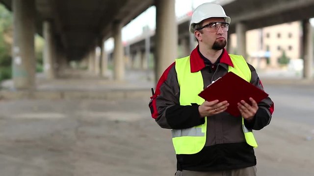 Road worker with work documentation. Building inspector with work documentation at project site under overpass