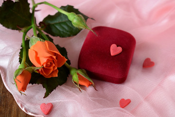 An orange rose and a box for jewellery on a pink cloth