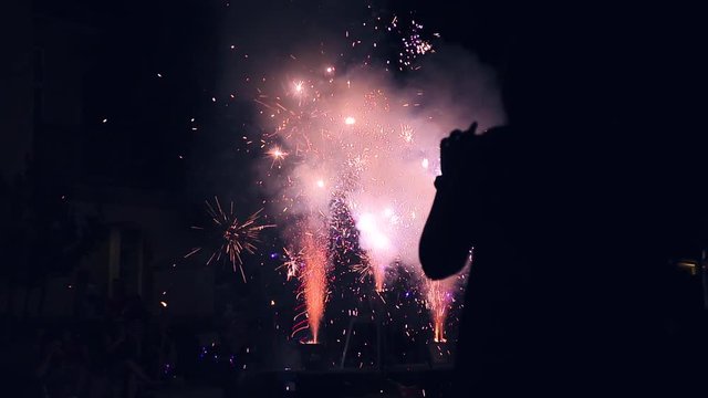 Silhouetted woman filming fireworks on smart phone. 