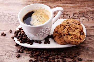 Coffee cup with chocolate cookies and coffee beans on wooden background