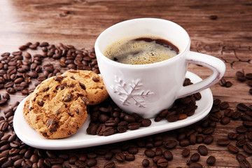 Coffee cup with chocolate cookies and coffee beans on wooden background