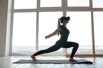 A young beautiful girl in virtual reality glasses makes yoga and aerobics remotely. Future technology concept. Modern imaging technology. Classes in single sports remotely.