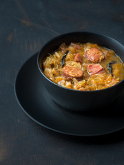 Cabbage soup in black plate on dark background. Copy space. 